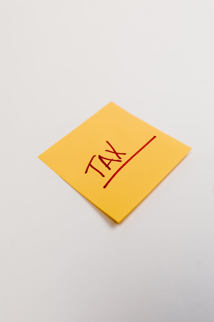 Yellow sticky note on white background with the word 'Tax' in red ink, ideal for finance concepts.
